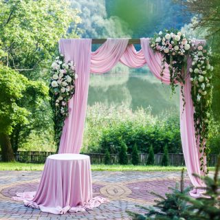 Pink wedding arch with floral white and pink decorations outside in green summer garden